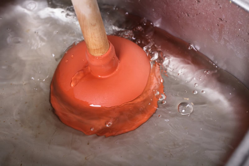 What Causes sewage Backup? An Orange Cup Plunger In The Washbasin Filled With Water.