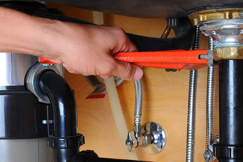 2025 Guide to Garbage Disposals. Photo of a technician performing maintenance on a garbage disposal.
